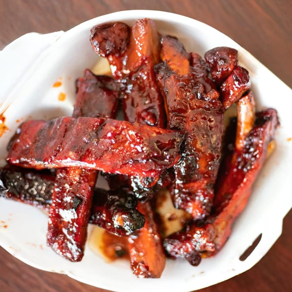 Sweet and sticky Chinese-style spare ribs, glistening with sauce, served in a white takeout container.
